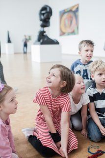 Kinder mit neugierigen Blicken sitzen in einer Ausstellung auf dem Boden.
