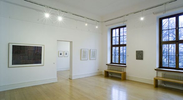 Ein großer heller Ausstellungsraum des Museums mit zwei großen Fenstern. An den Wänden befinden sich Ausstellungsstücke.