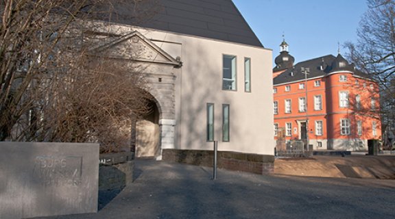 Bick auf das weiße Portal von Schloss Wissem. Im Hintergrund sieht man Teile des roten Museumsgebäudes.