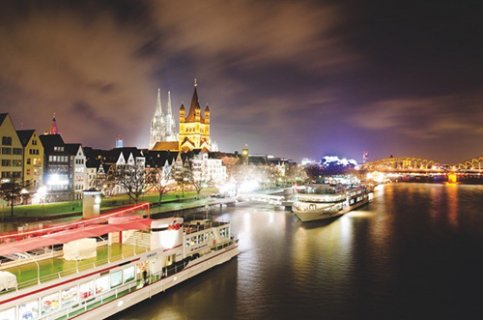 Schiffe liegen bei Nacht vor der spektakulär beleuchteten Kölner Altstadt.