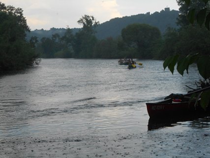 Auf dem Fluss fahren in der Abenddämmerung zwei Kanus. Ein weiteres Boot hat am Ufer festgemacht.