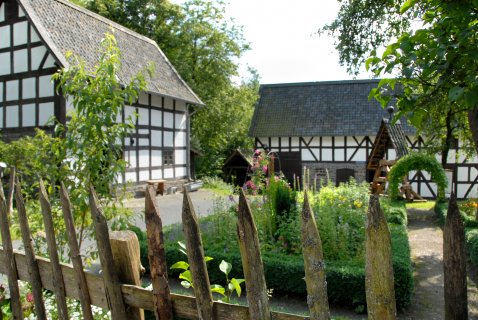 Ein alter Fachwerkhof mit zwei Häusern, einem Garten und einem Brunnen im Hof.