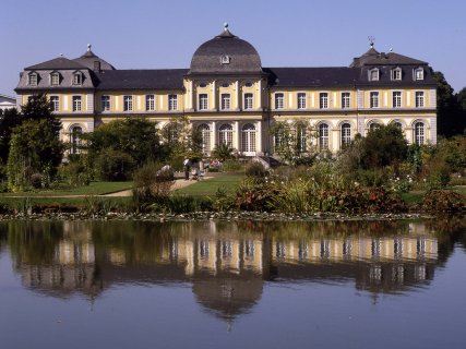 Frontalansicht des Poppelsdorfer Schlosses, das sich auf einer großen Wasserfläche spiegelt. 